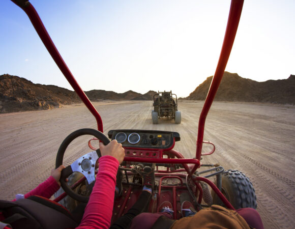 Cropped Image Of Tourists Riding Beach Buggies On Dessert Against Clear Sky